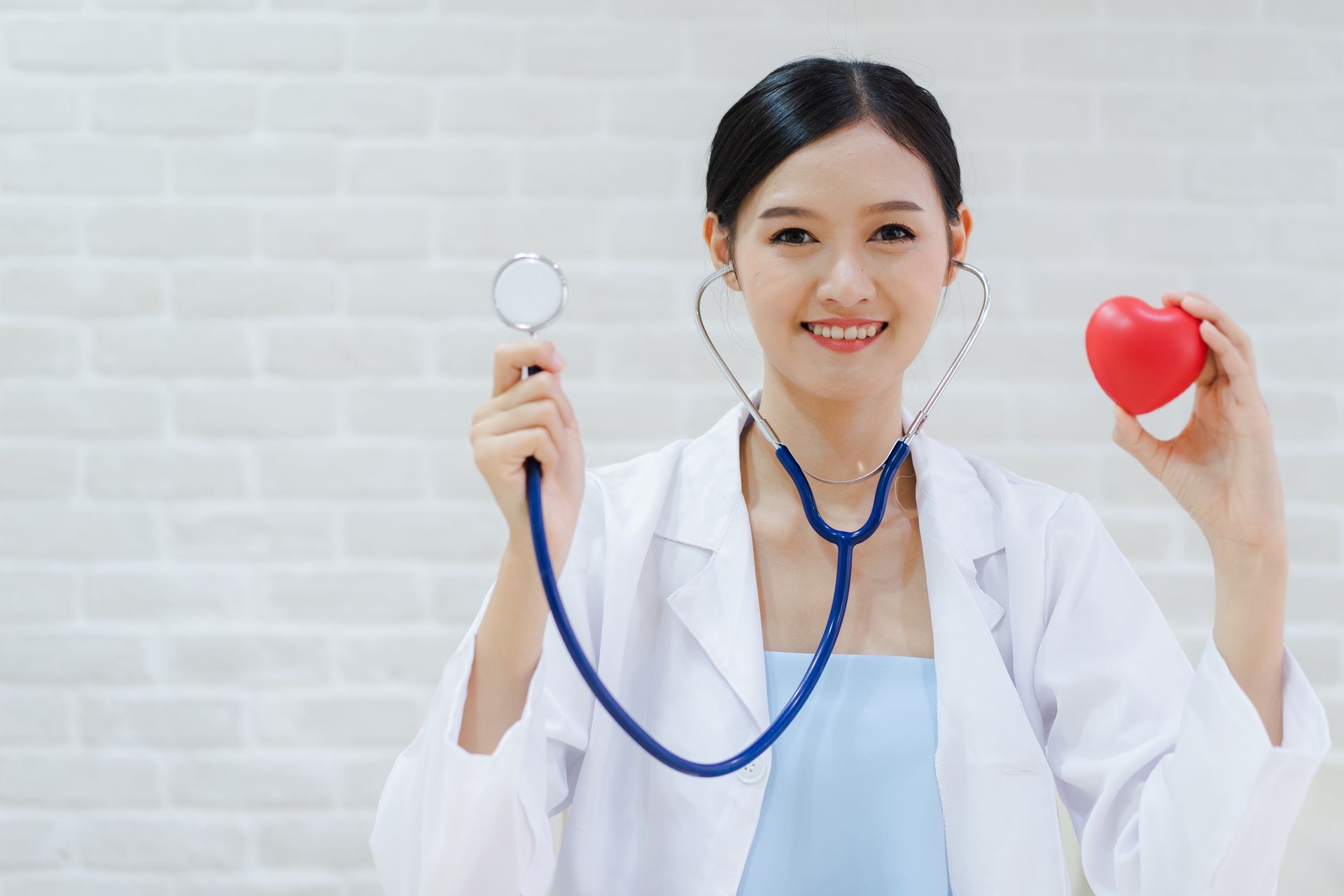 Young woman doctor holding a red heart, standing on brick wall background